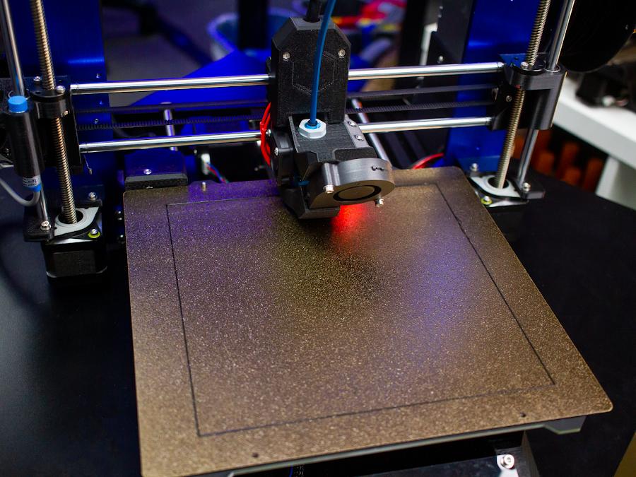 A 3D printer prints a gold-colored object.