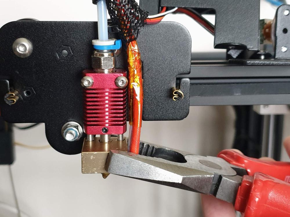 A photo of a person using pliers to remove the nozzle from a 3D printer.