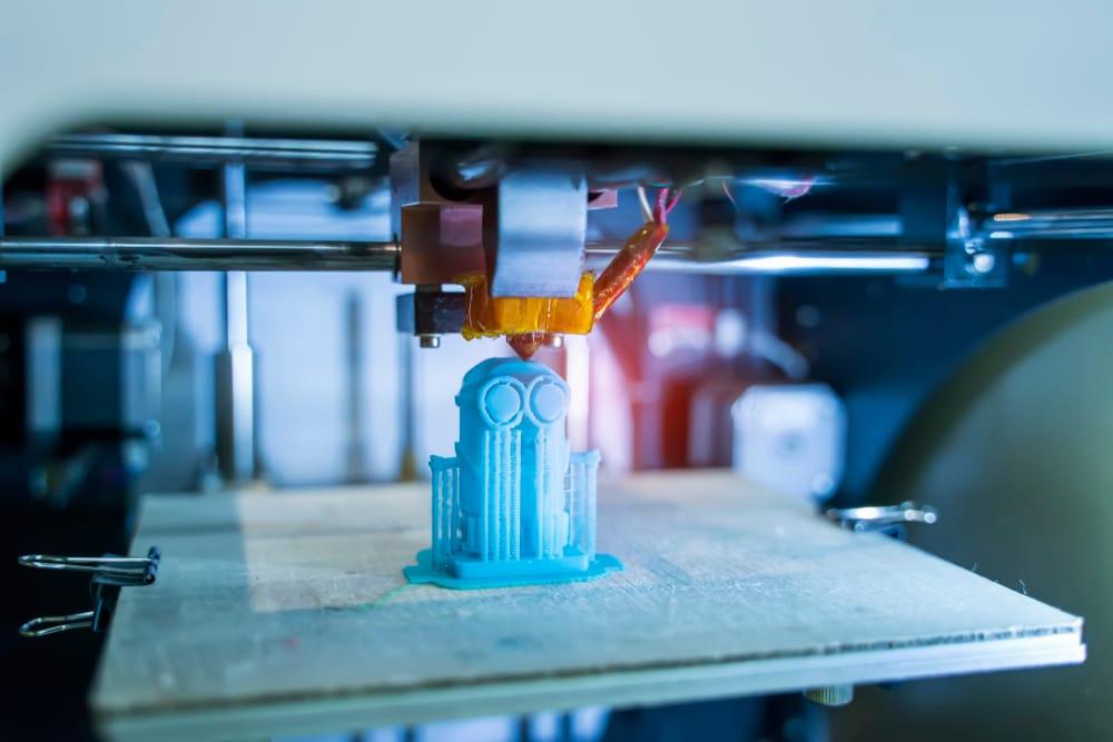 A 3D printer is printing a blue plastic figurine.