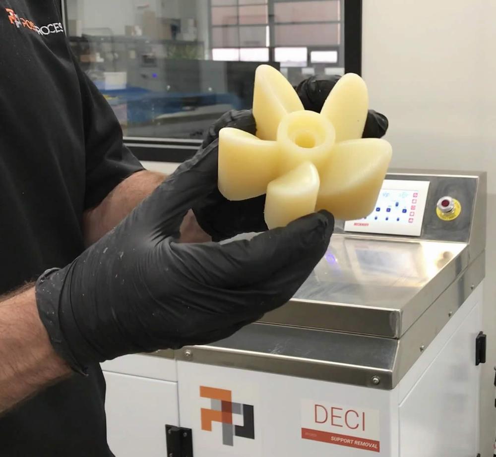 A gloved hand holds a 3D printed impeller made of yellow plastic.