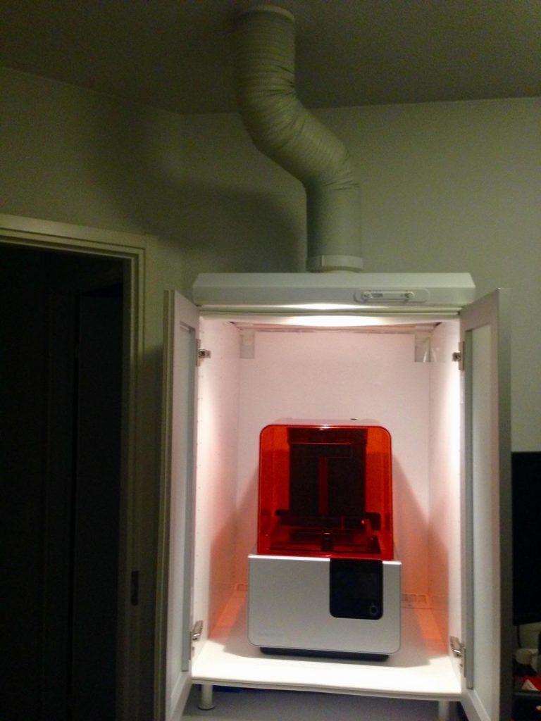 An orange 3D printer sits inside a white cabinet.