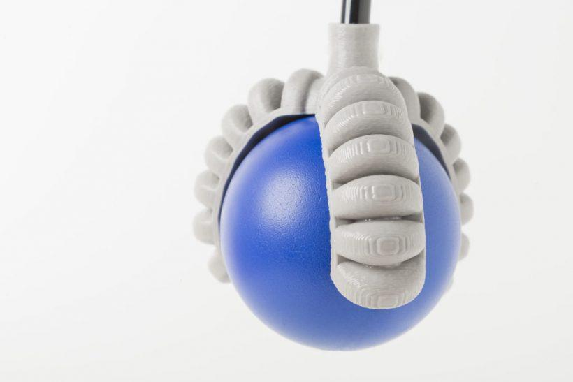 A blue ball is held in a gray, 3D printed hand.