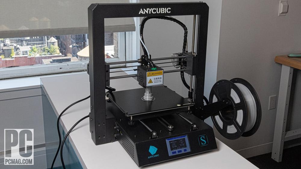 A black and blue Anycubic 3D printer is printing a white object on a glass print bed.