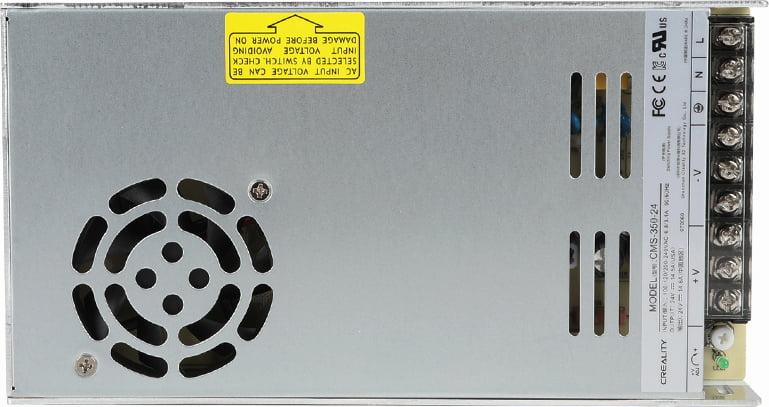 The image shows a silver power supply with a black fan on the left and a label on the right.