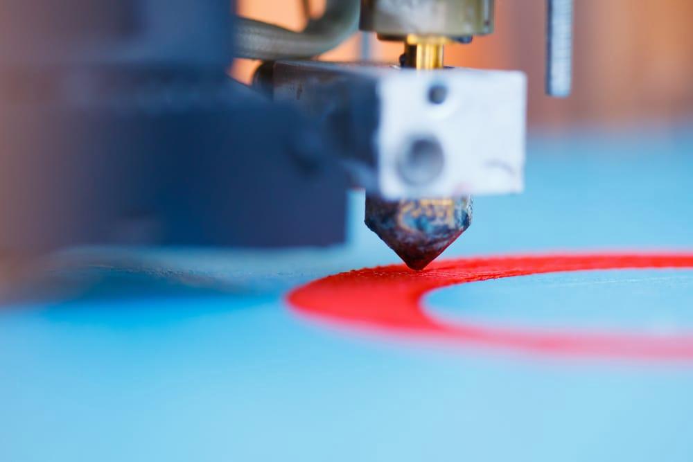 A close-up of a 3D printer printing a red circle on a blue surface.