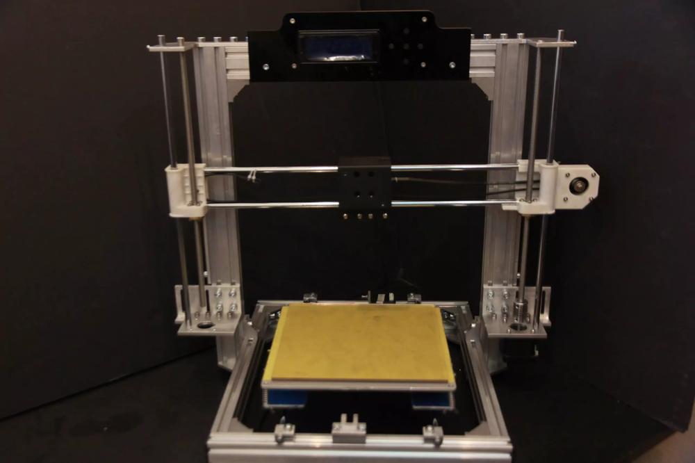 A 3D printer with a black frame and a yellow print bed.
