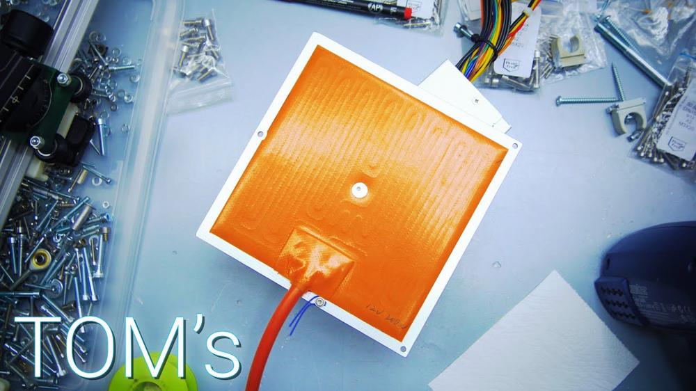 A photo of a 3D printer heatbed with an orange magnetic PEI sheet on top of it.