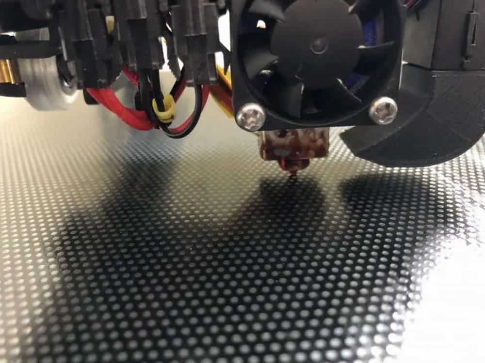 Close-up of a 3D printer nozzle extruding molten plastic onto a textured print bed.