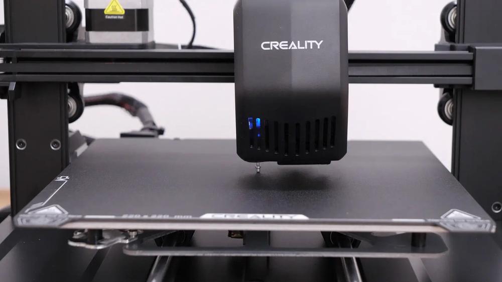 A close-up of a 3D printers nozzle positioned above a black print bed.