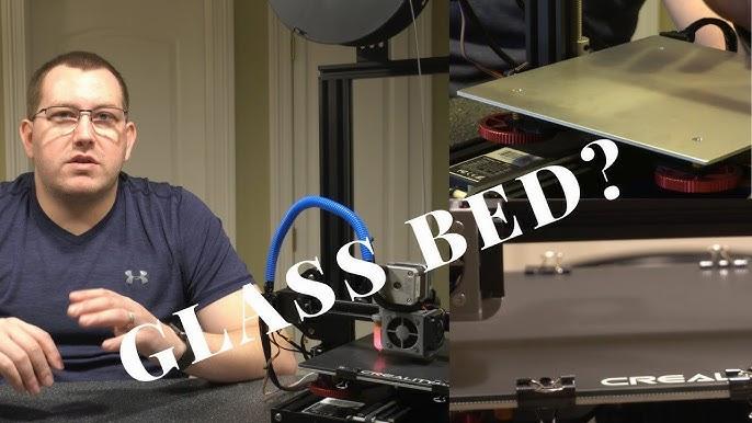 A man is talking to the camera about 3D printers while standing next to a Creality Ender 3 Pro 3D printer with a glass bed upgrade.