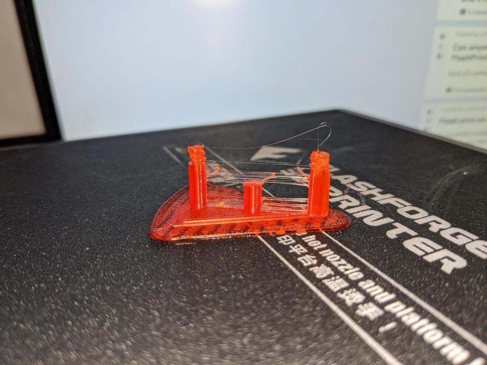 A 3D printed orange plastic part with supports still attached.