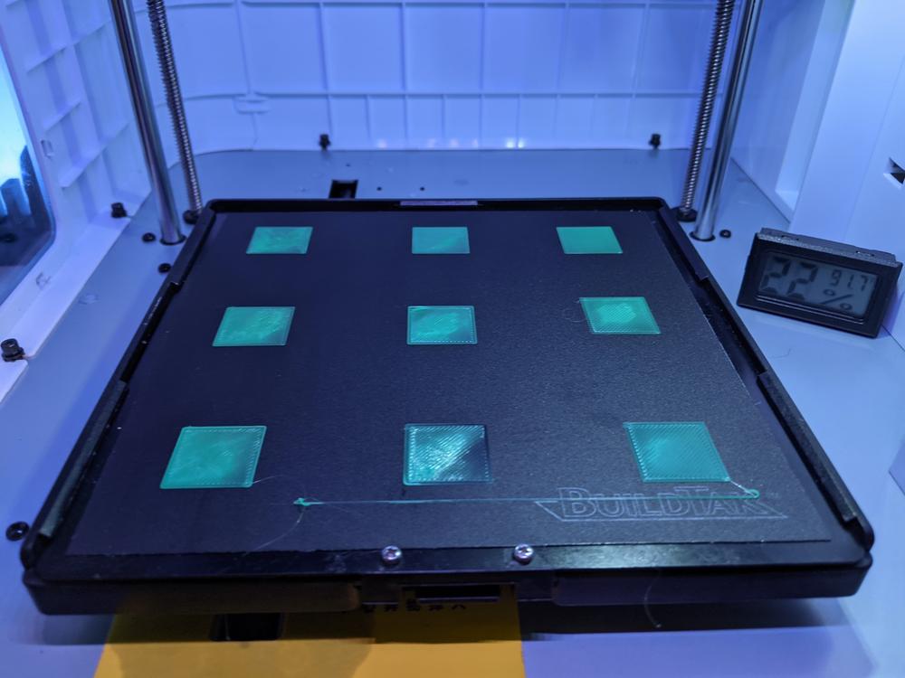 3D printed squares of varying sizes sit on a 3D printer bed with a thermometer reading 29 degrees Celsius in the corner.