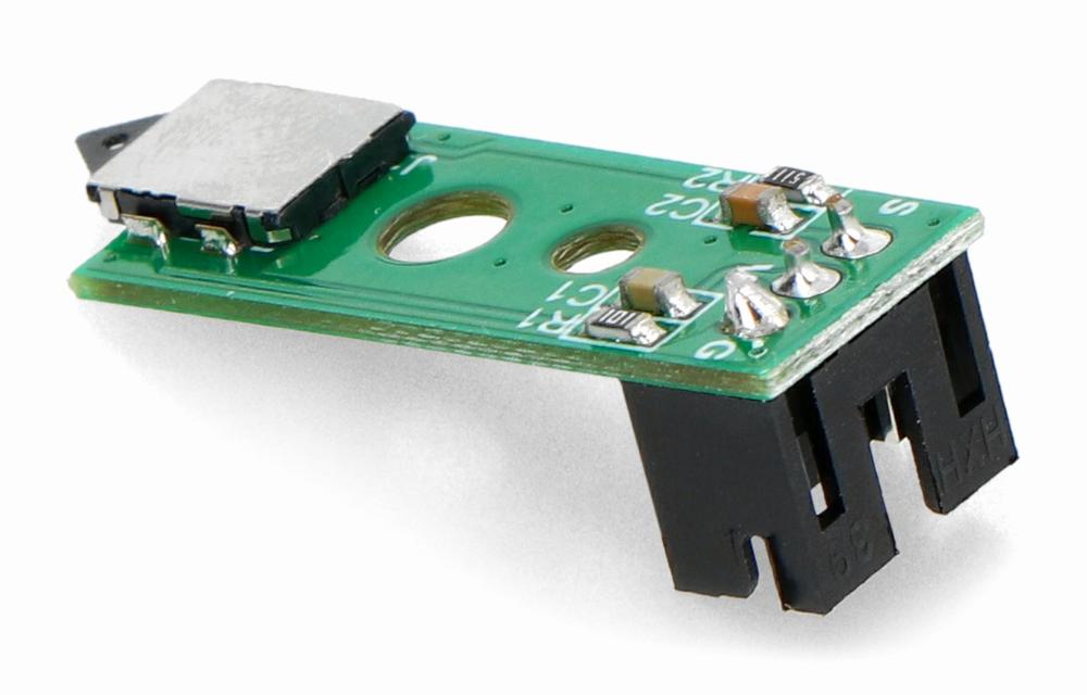 A small green circuit board with a black connector on one end and a small white button on the other.