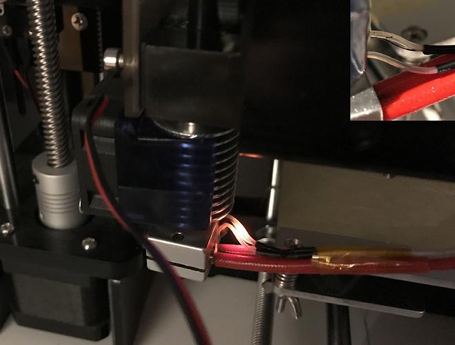 Close-up of a 3D printers hot end with a red silicone sock and exposed wiring.