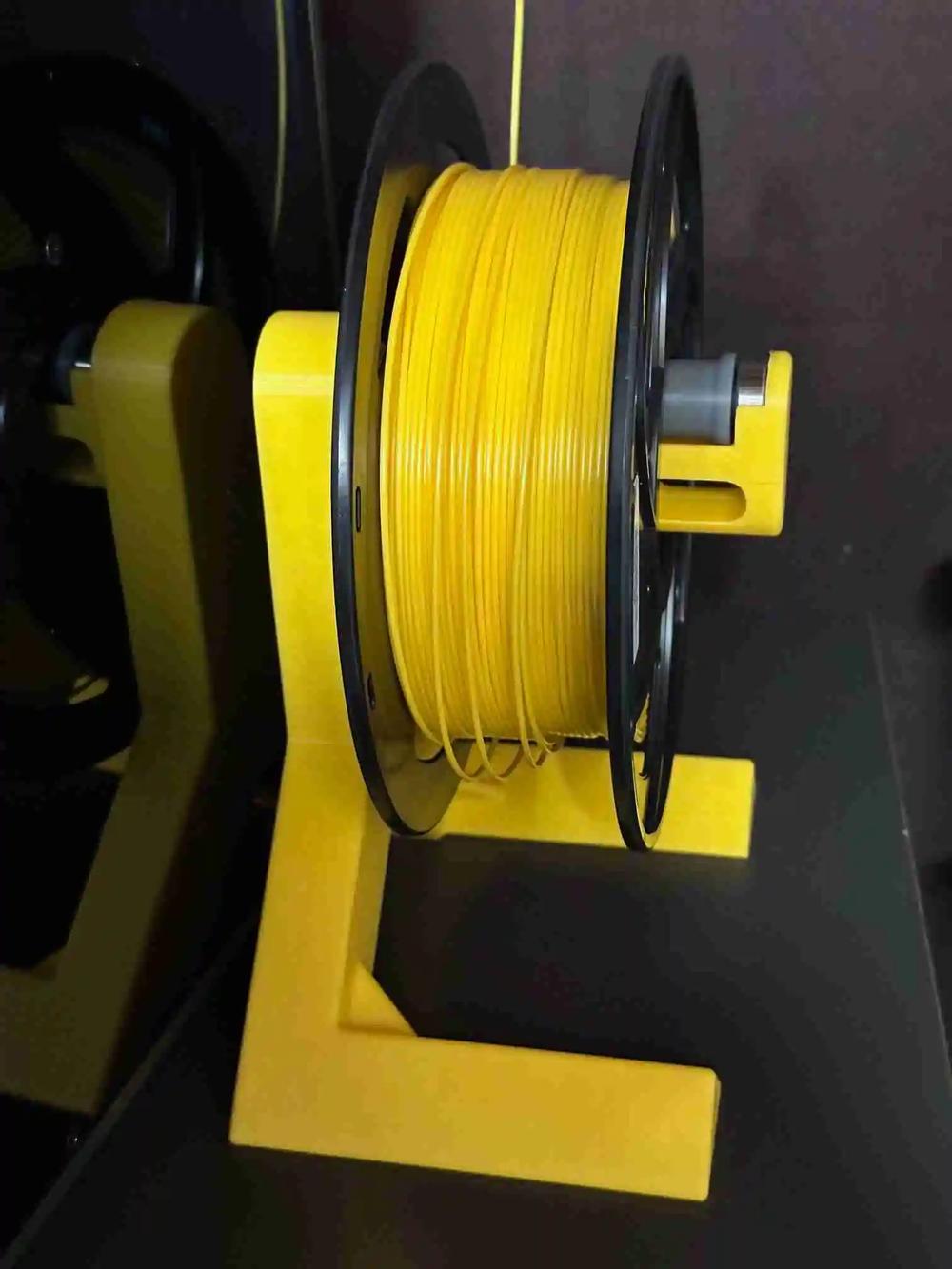 A yellow plastic spool holder for 3D printers, holding a spool of yellow filament.