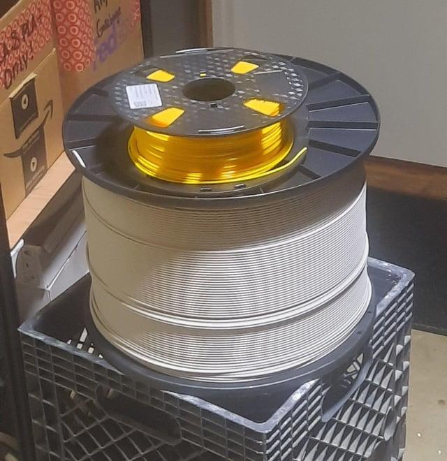 A large spool of yellow filament sits on a black plastic crate.