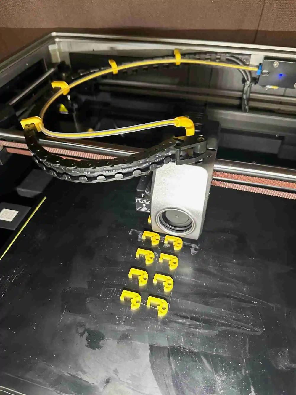 A 3D printer is printing a series of small, yellow plastic letters F.