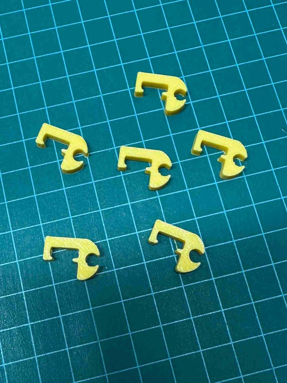 Several 3D printed yellow pound symbols scattered on a green cutting mat.