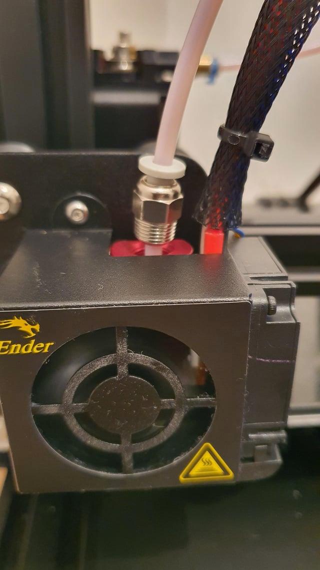 A white Bowden tube is connected to a black 3D printer hot end.