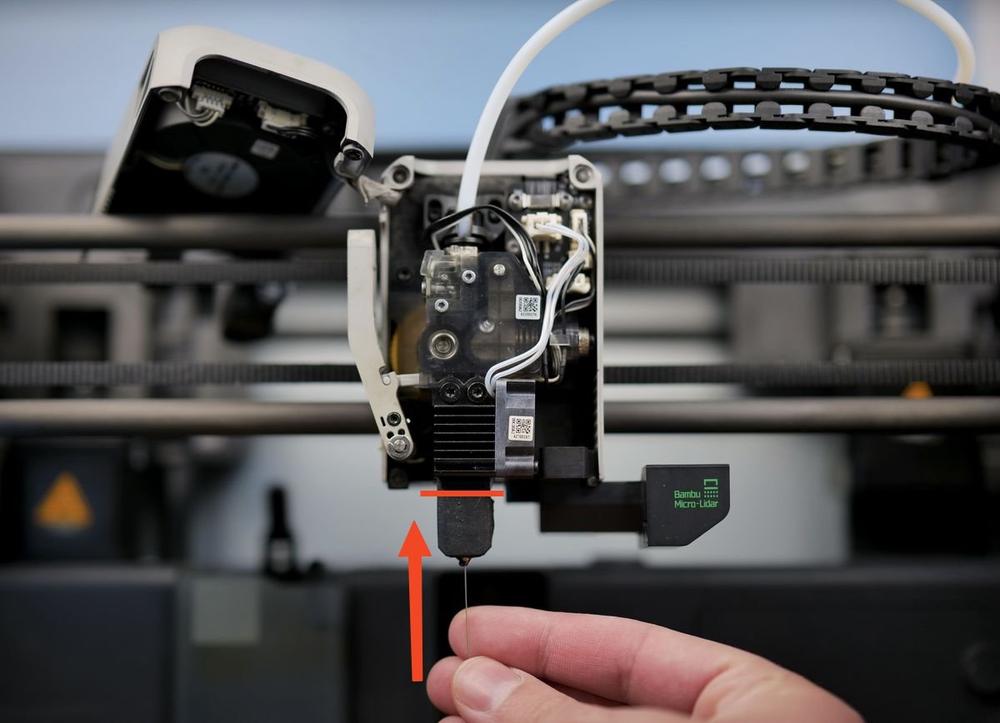 A finger is pointing at a black nozzle on a 3D printer.