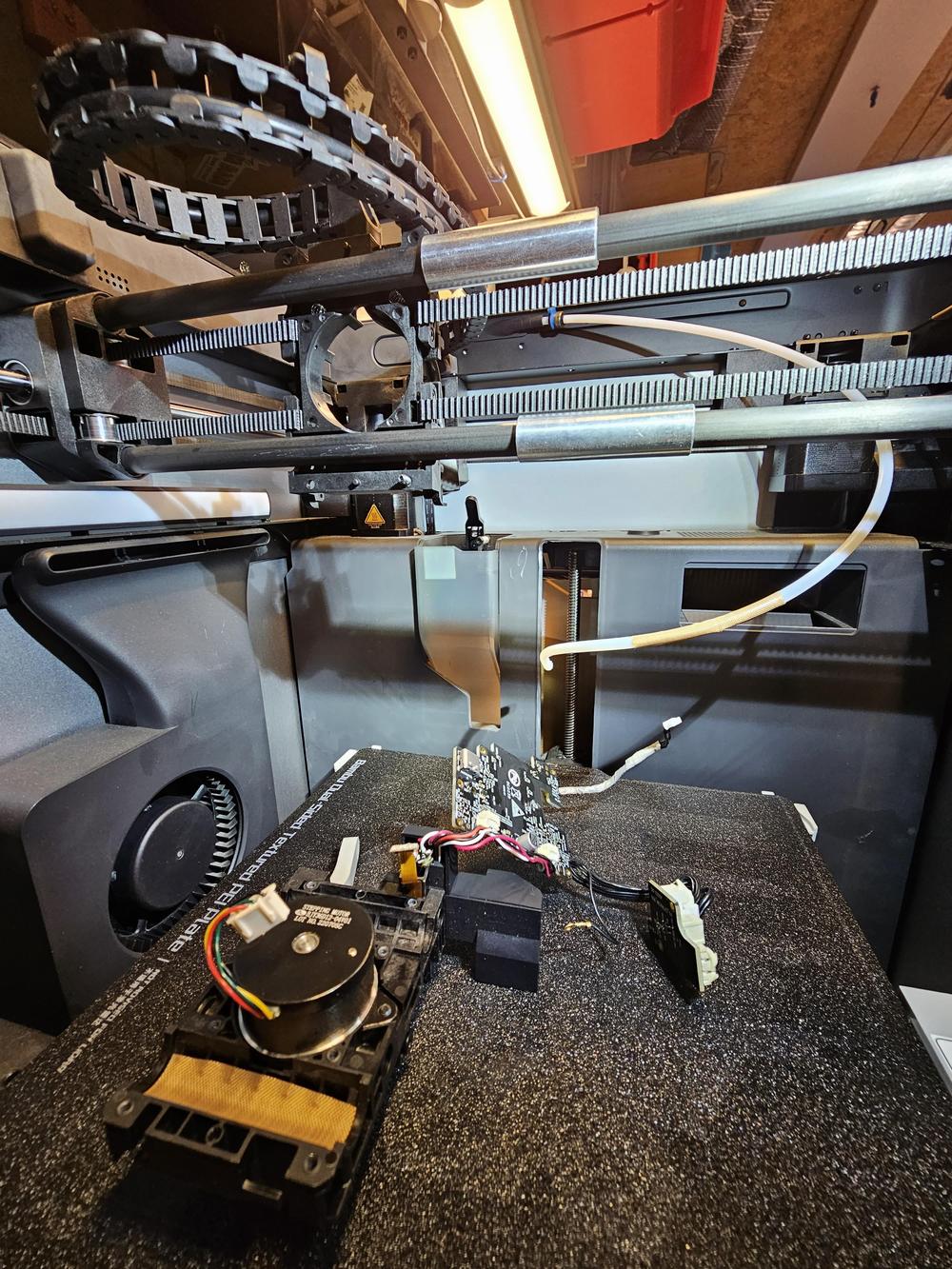 A 3D printer with its cover removed and a circuit board exposed.
