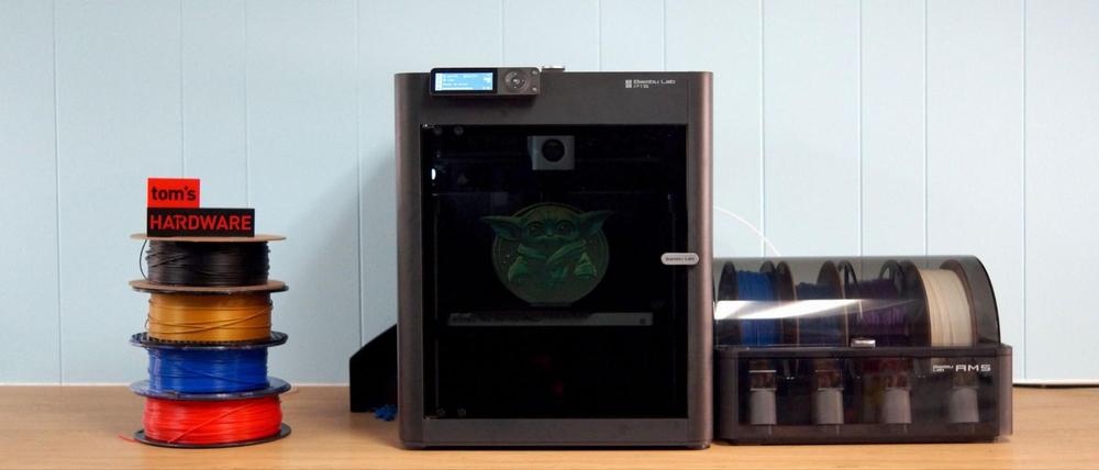 A 3D printer is printing a green Yoda head, with a stack of filament spools next to it.