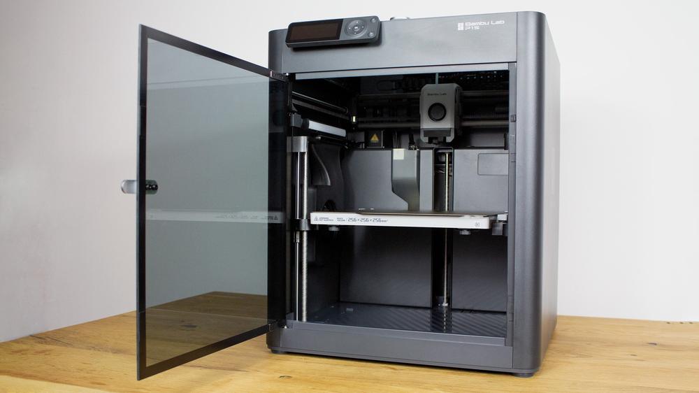 The image shows an open black 3D printer with a glass door.
