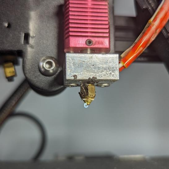 Close-up of a 3D printer nozzle with a drop of molten plastic on the tip.