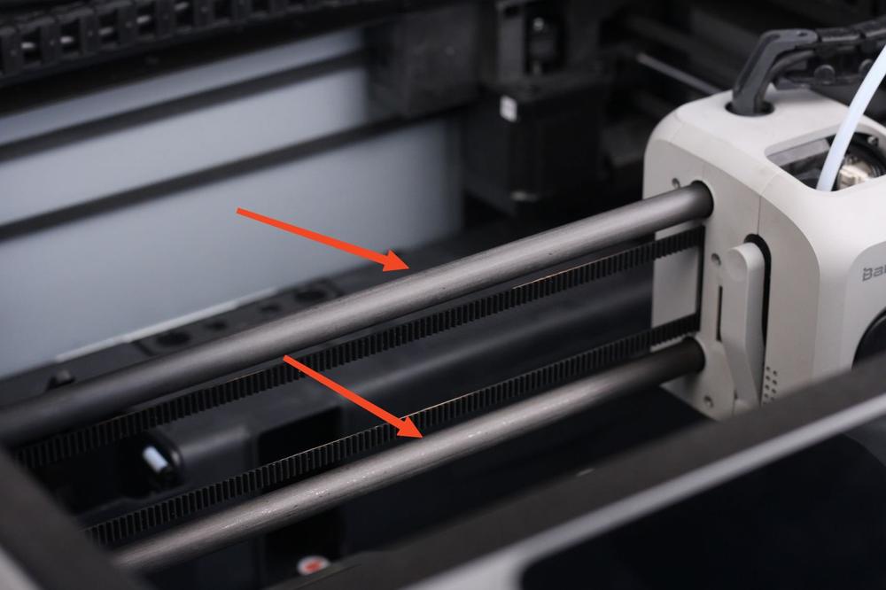 Two arrows point to a black, toothed belt on a 3D printer.