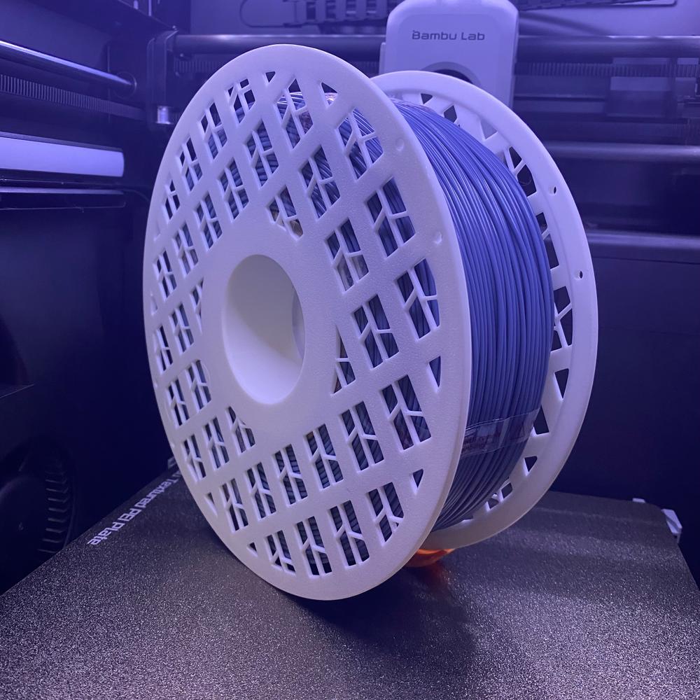 A spool of blue filament sits on a white 3D printer.