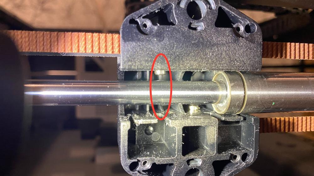 A metal rod inside a 3D printer, with a red circle around a small wheel attached to the rod.