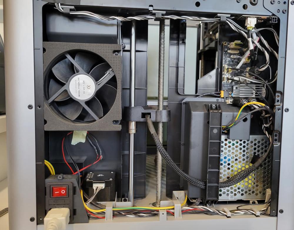 The image shows the inside of a 3D printer with a cooling fan, power supply, and circuit board.