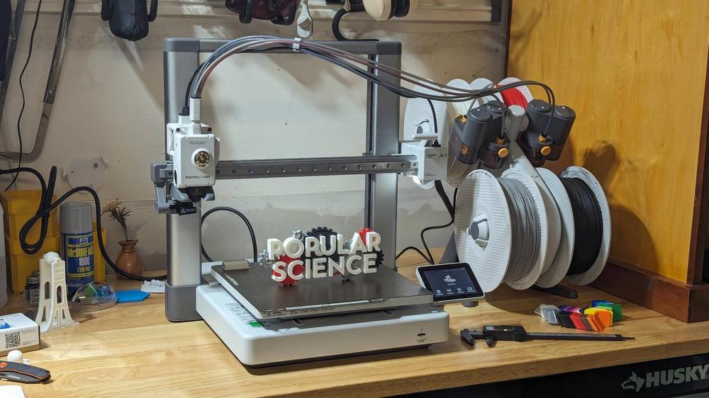 A 3D printer is printing a red and white sign that says Popular Science.