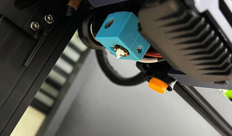 A blue 3D printed part is attached to the metal extruder of an Ender 3 V2 3D printer.