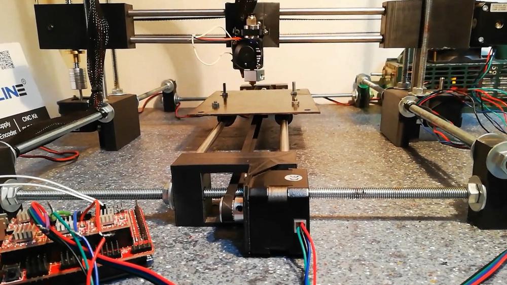 A 3D printer is printing a black object on a metal bed.