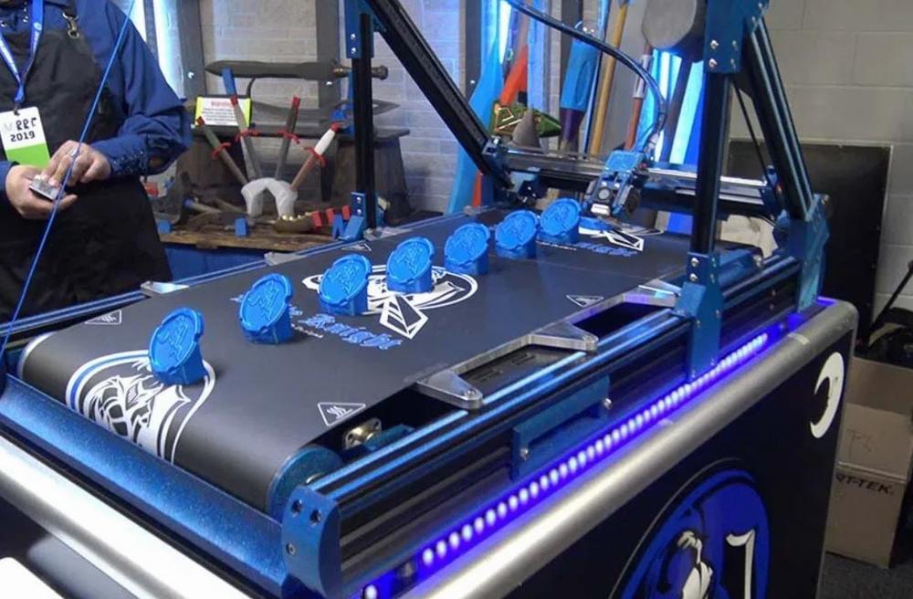A 3D printer prints out several small blue objects on a blue platform.