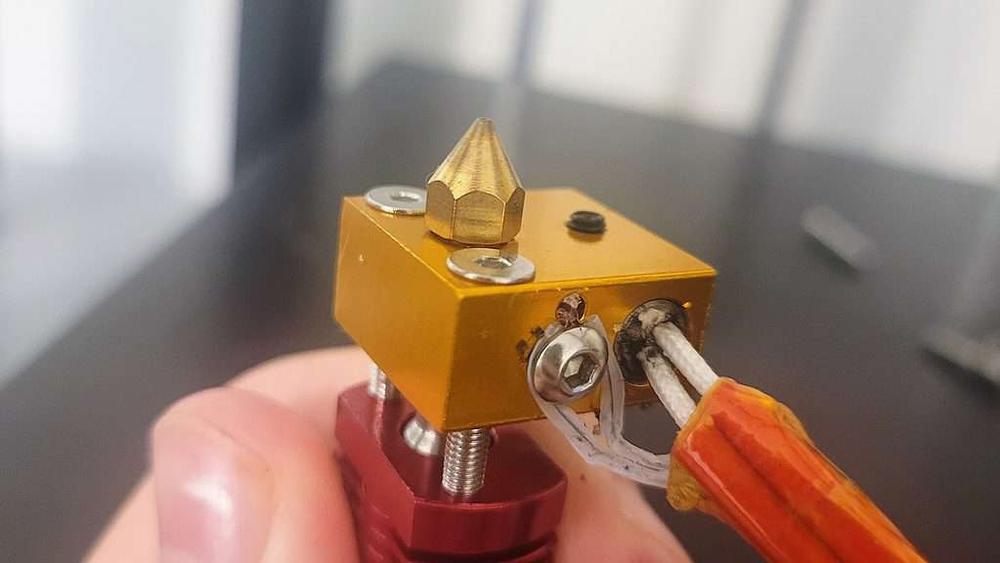 A close up of a brass nozzle on a 3D printer hot end.