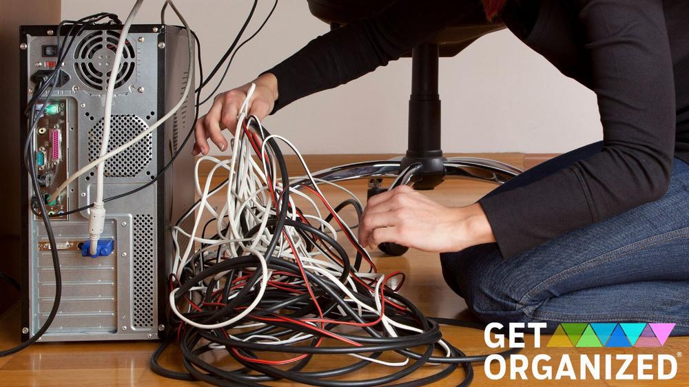 A person is kneeling on the floor next to a computer tower, with a lot of loose cables next to it.