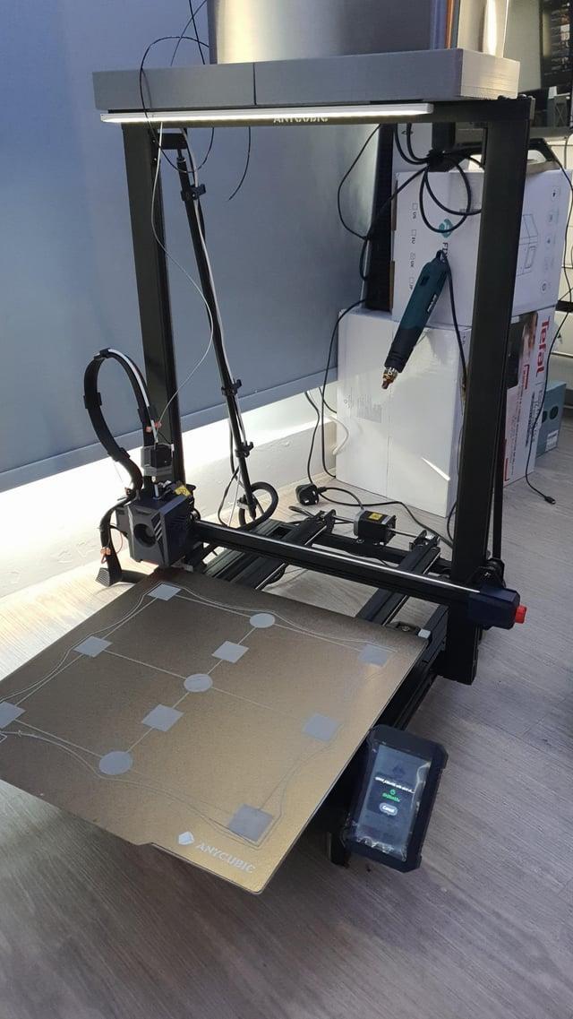 A black and grey 3D printer sits on a table with a nearly finished 3D print on the print bed.