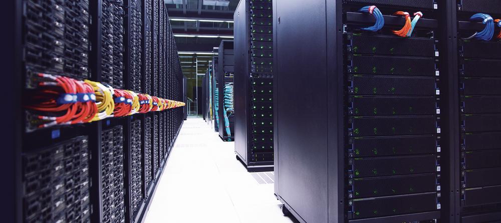 A long, narrow room filled with rows of tall black server cabinets with blinking lights and colorful cables.
