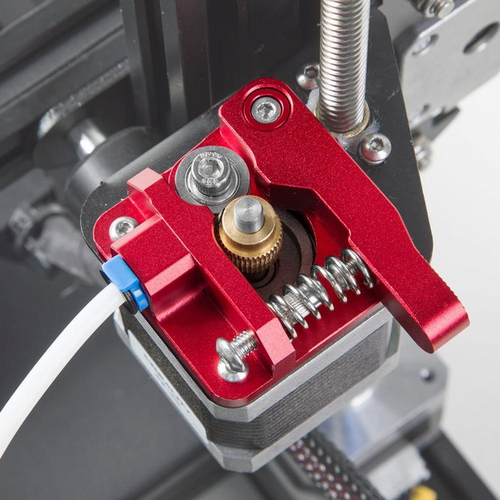 A close up of a red metal extruder with a white filament tube attached.