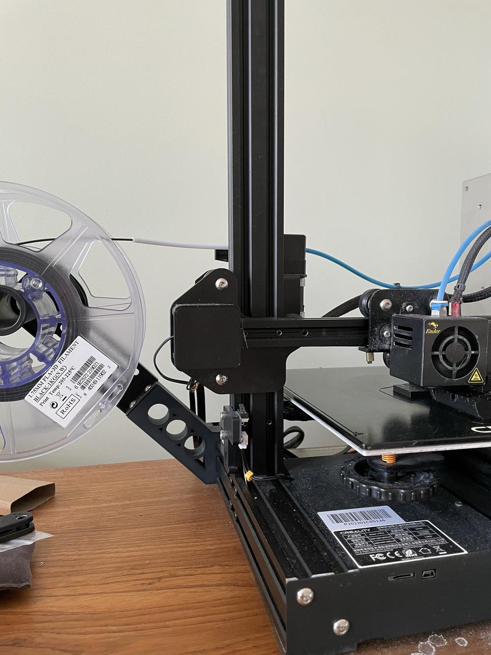 A black spool of 3D printer filament is loaded into a 3D printer.