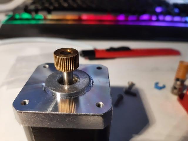 A close up of a brass gear attached to a silver stepper motor.