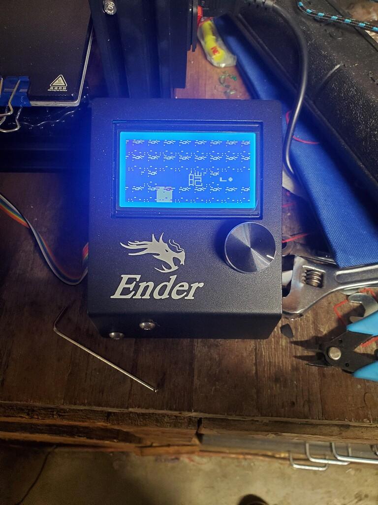 A blue screen on a black 3D printer displays a pixelated image of a dragon.
