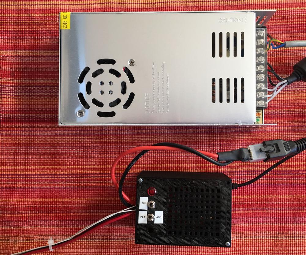 A photo of the back of a desktop computer power supply and a 3D printed case with a power switch and a small fan.