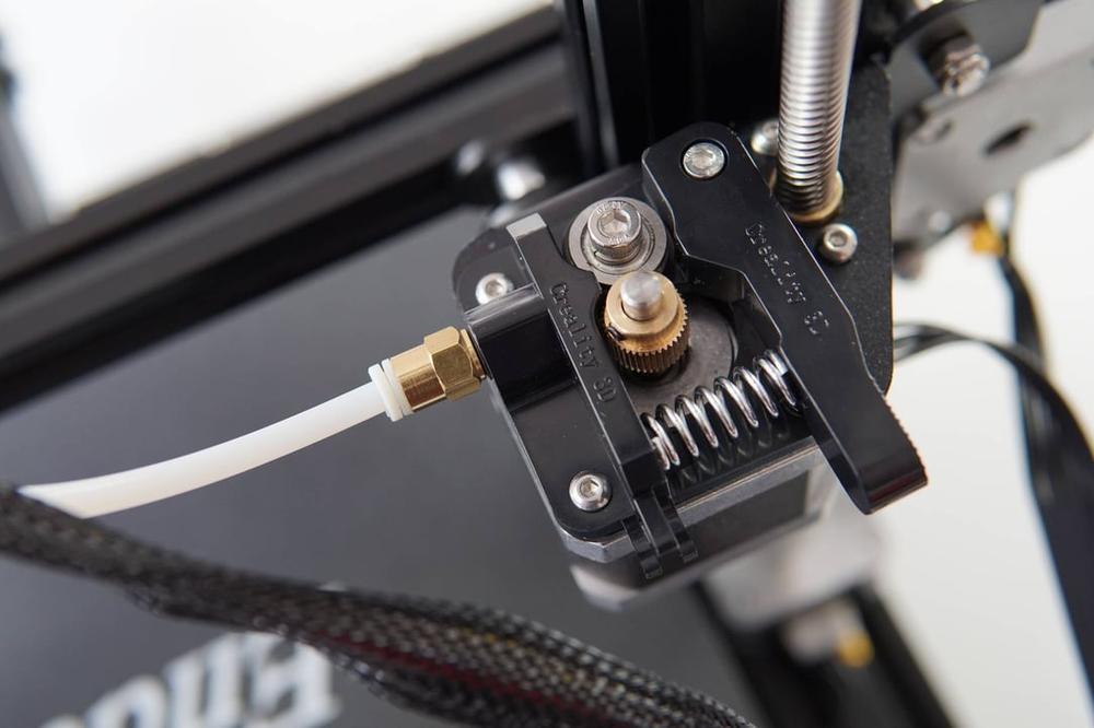 A close-up of a black metal extruder with a white Bowden tube attached.