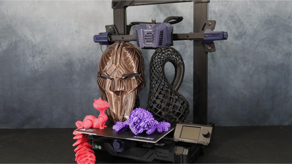 A 3D printer is printing a variety of objects, including a mask, a squirrel, and a coral reef.