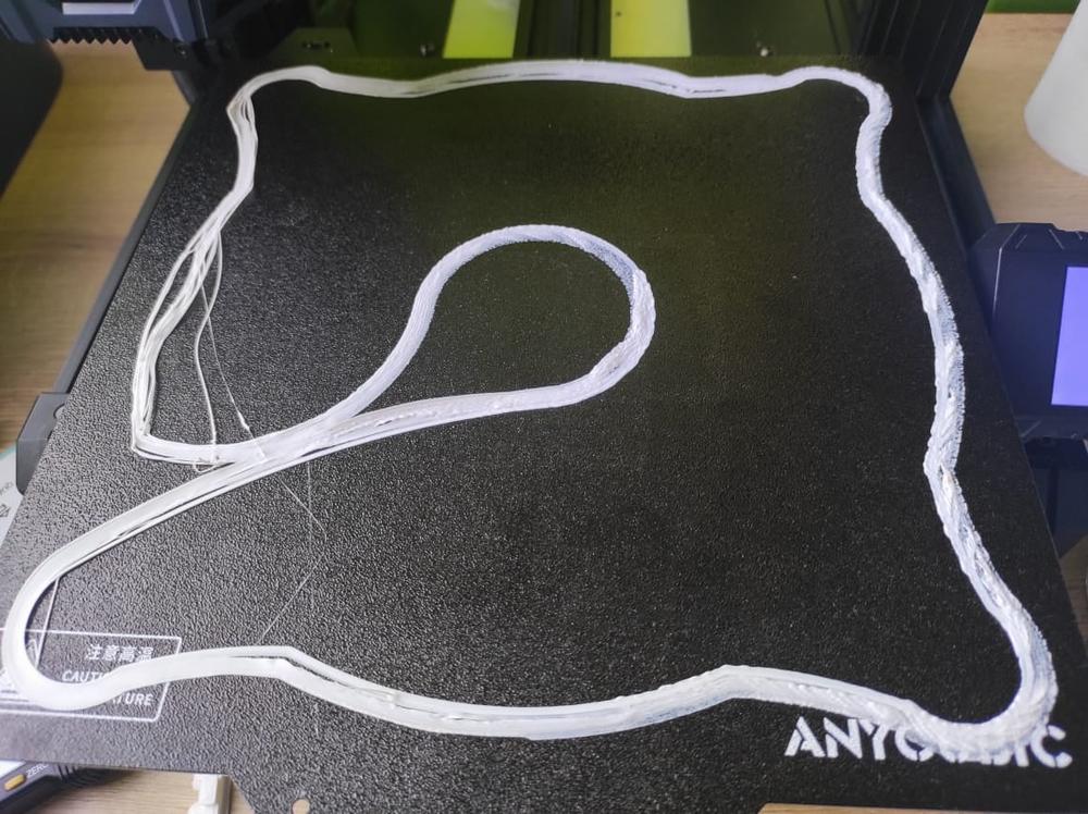 A 3D printer is printing a white plastic object on a black print bed.