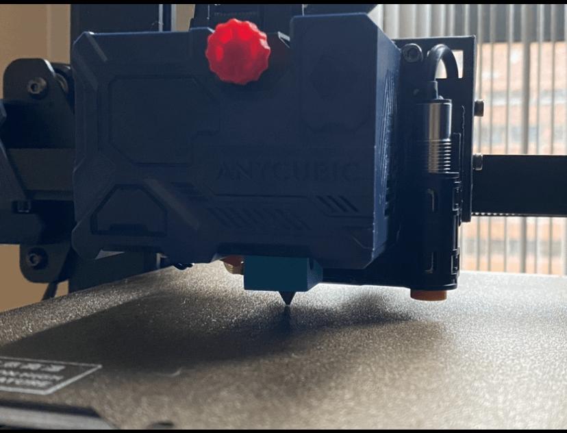 Close-up of a 3D printer nozzle above a black print bed.