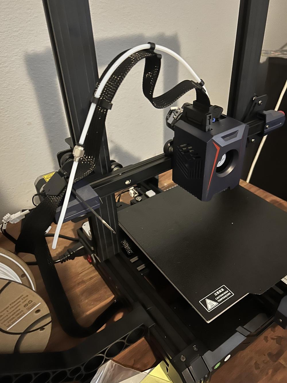 A 3D printer with a black frame and a red nozzle is printing a white object.